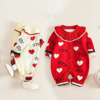 Two baby outfits, one red with white hearts and text, the other cream with red hearts and text, on a light background.