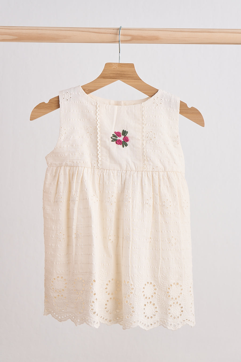 Beige sleeveless dress with floral embroidery on a wooden hanger against a white background
