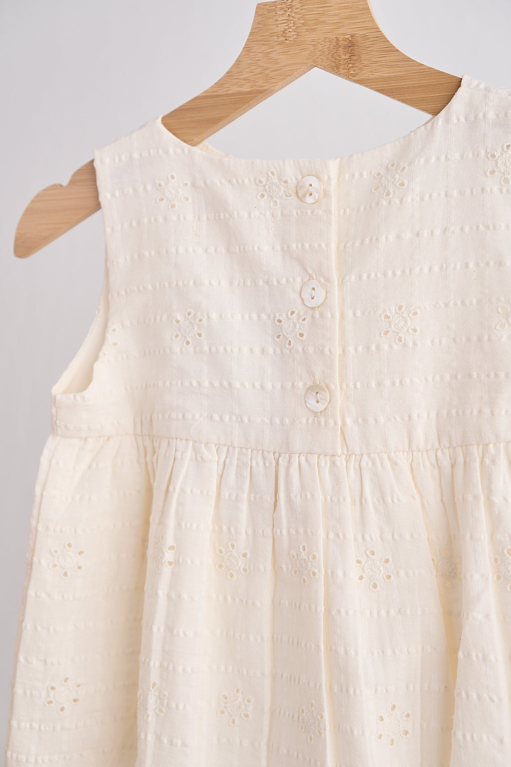 White sleeveless dress on a wooden hanger against a light gray background