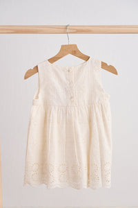 White sleeveless dress on a wooden hanger against a light gray background