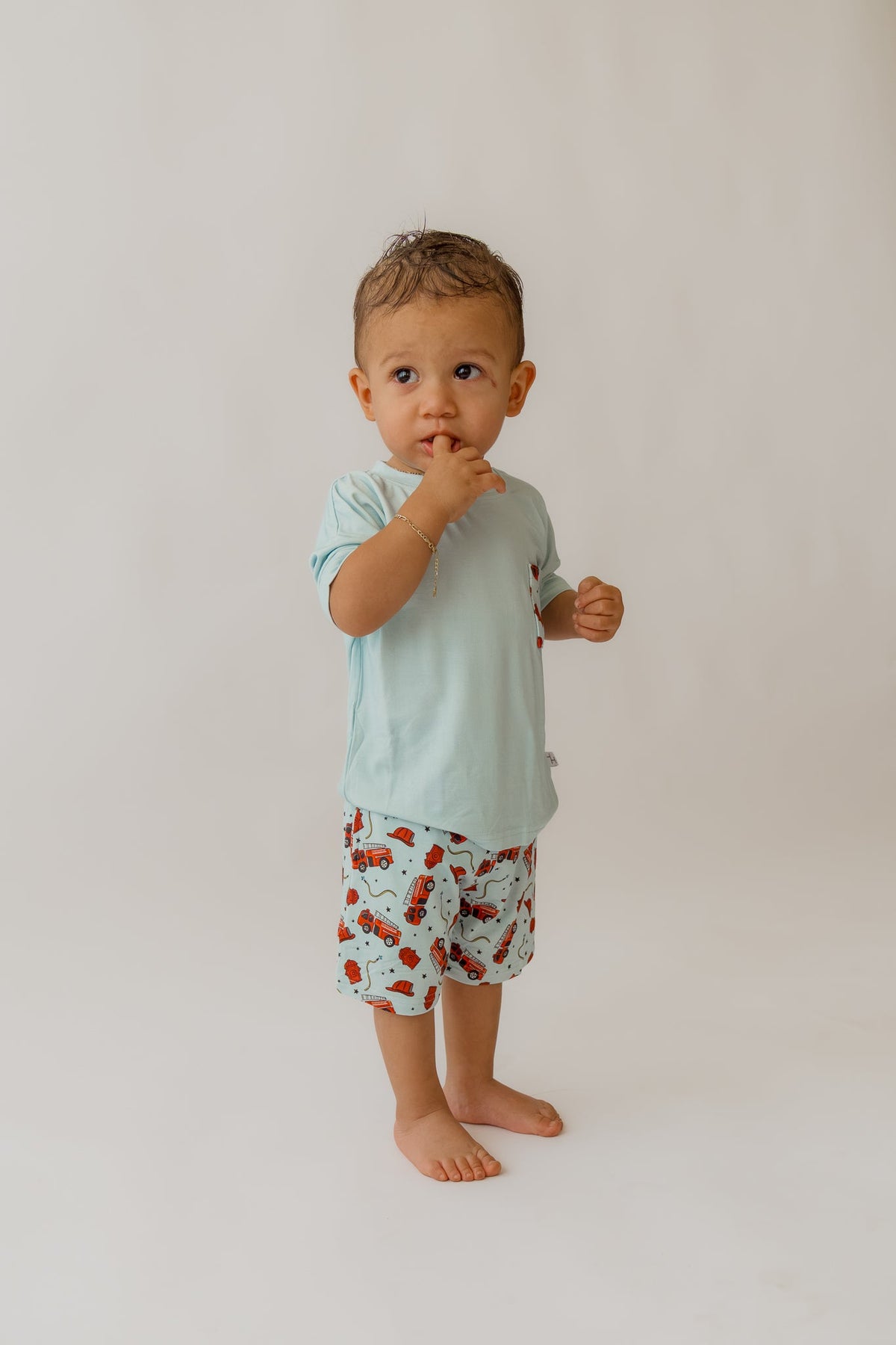 Toddler in light blue bamboo lounge set with red fire truck print shorts against white background