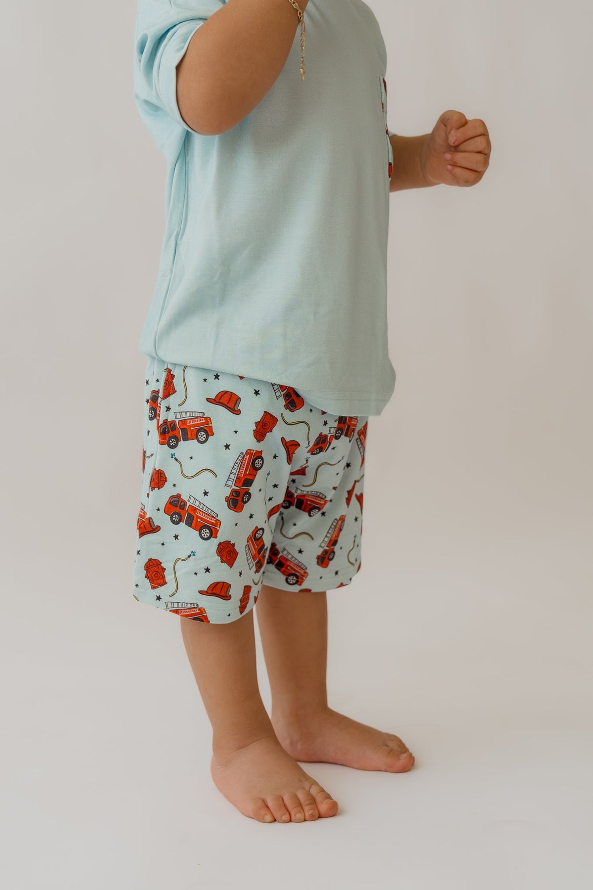Side view of toddler wearing drop-shoulder light blue shorts with vibrant red fire engine pattern