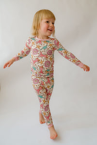 Smiling blonde toddler in cream mermaid print pajamas with pink cuffs