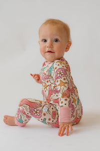 Seated baby displaying rear mermaid pattern on cream onesie with visible white size tag on inner leg seam