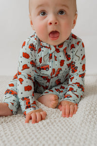 Baby crawling on white rug in light blue fire truck print onesie with red trucks and black stars