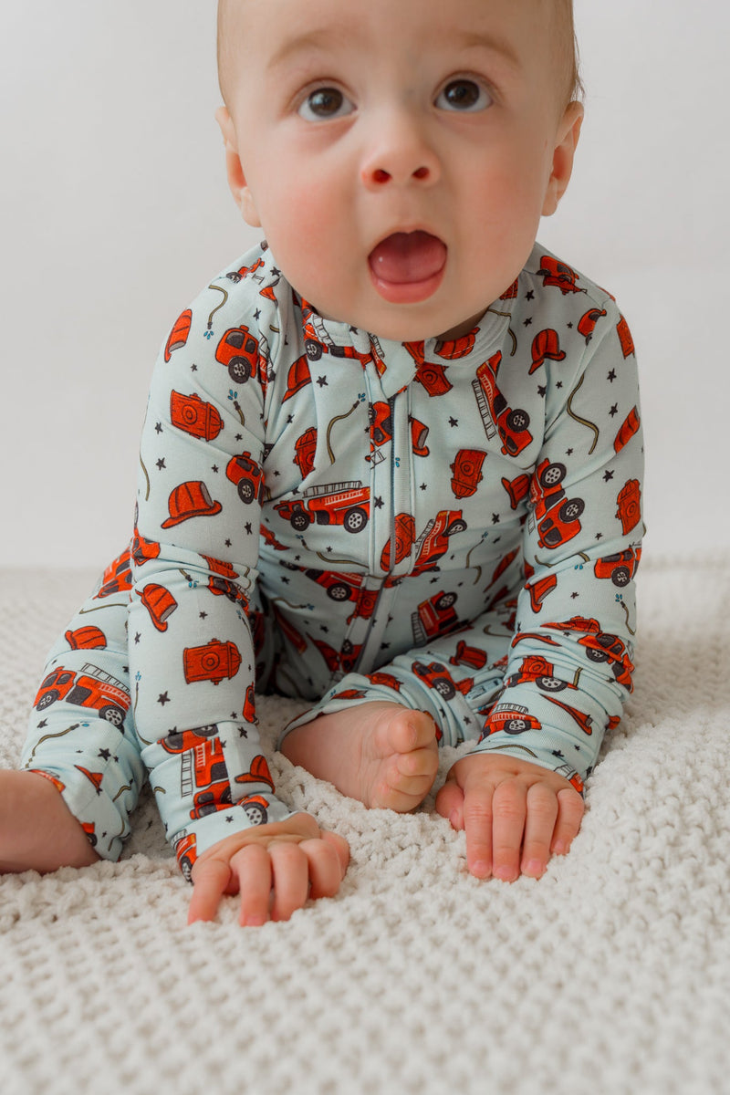 Baby crawling on white rug in light blue fire truck print onesie with red trucks and black stars