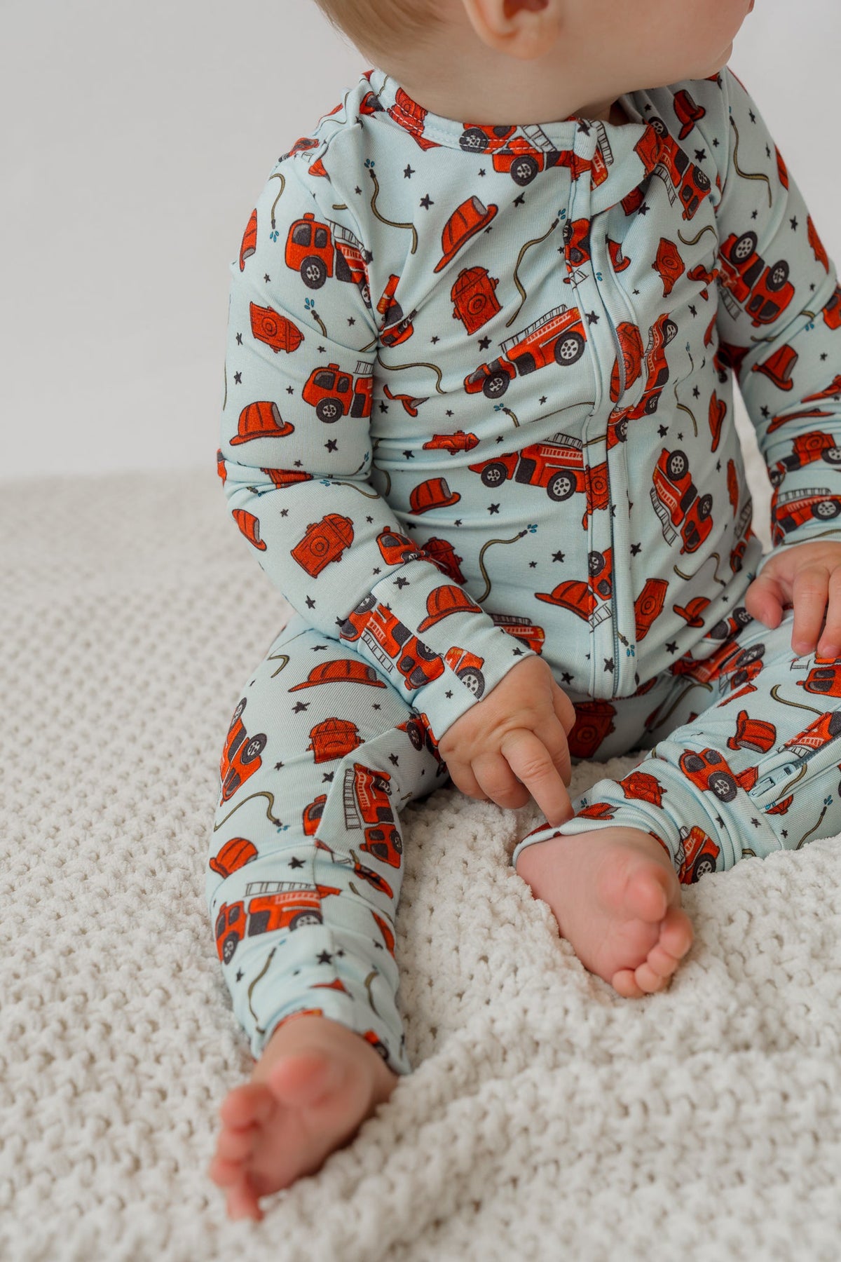 Close-up of light blue fire truck print baby romper showing stretchy fabric and convertible feet