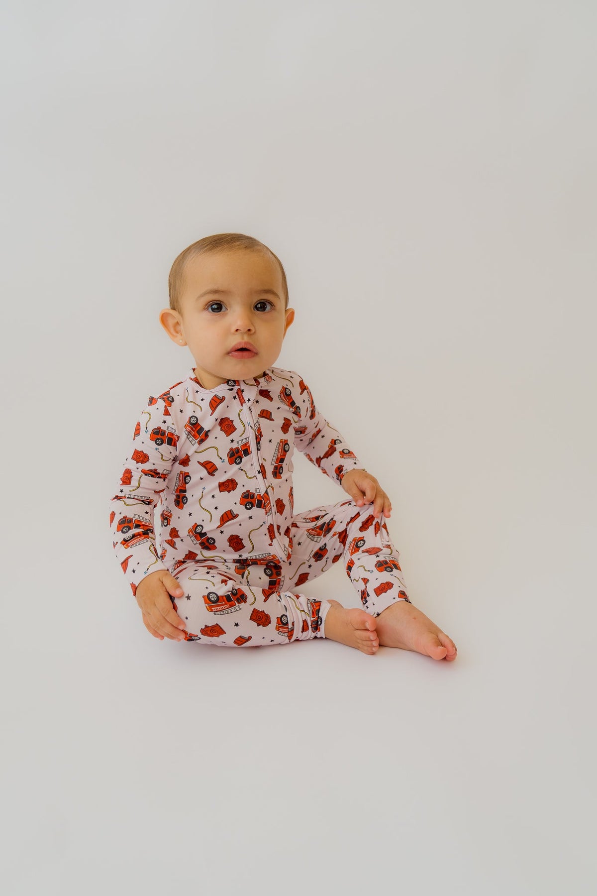 Baby in pink fire truck onesie with red trucks and black stars on white background