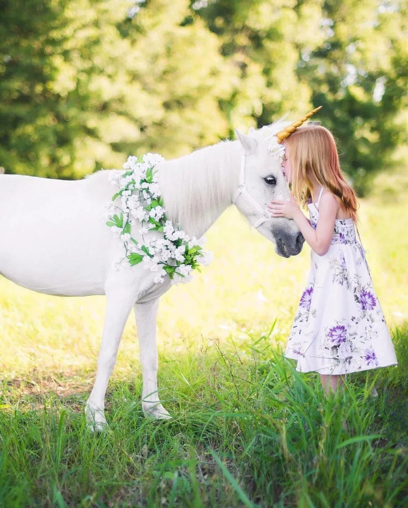 A young girl lovingly interacting with a unicorn, wearing the 'Oh Suzannah' Floral Party Dress in lavender.