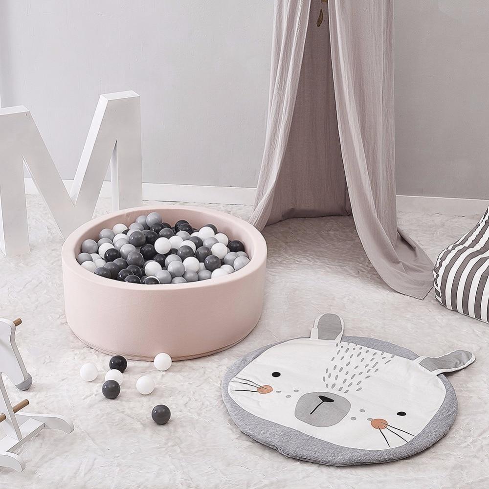 Children's play area with a pink ball pit, gray and white ball pit balls, and a gray and white animal-shaped mat on a light wooden floor.