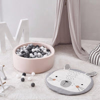 Children's play area with a pink ball pit, gray and white ball pit balls, and a gray and white animal-shaped mat on a light wooden floor.