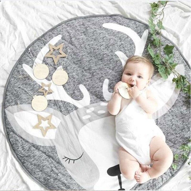 Baby lying on a round gray rug with deer antlers and stars, surrounded by greenery.