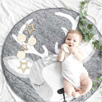 Baby lying on a round gray rug with deer antlers and stars, surrounded by greenery.