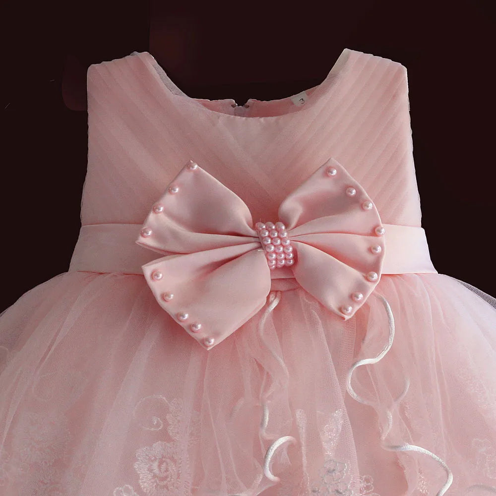 Pink newborn dress with pearl-bead bow, round neckline, and tulle skirt, zip-back.