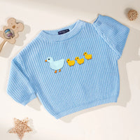 Baby blue pullover with ribbed cuffs showing mother duck embroidery near wooden bear rattle