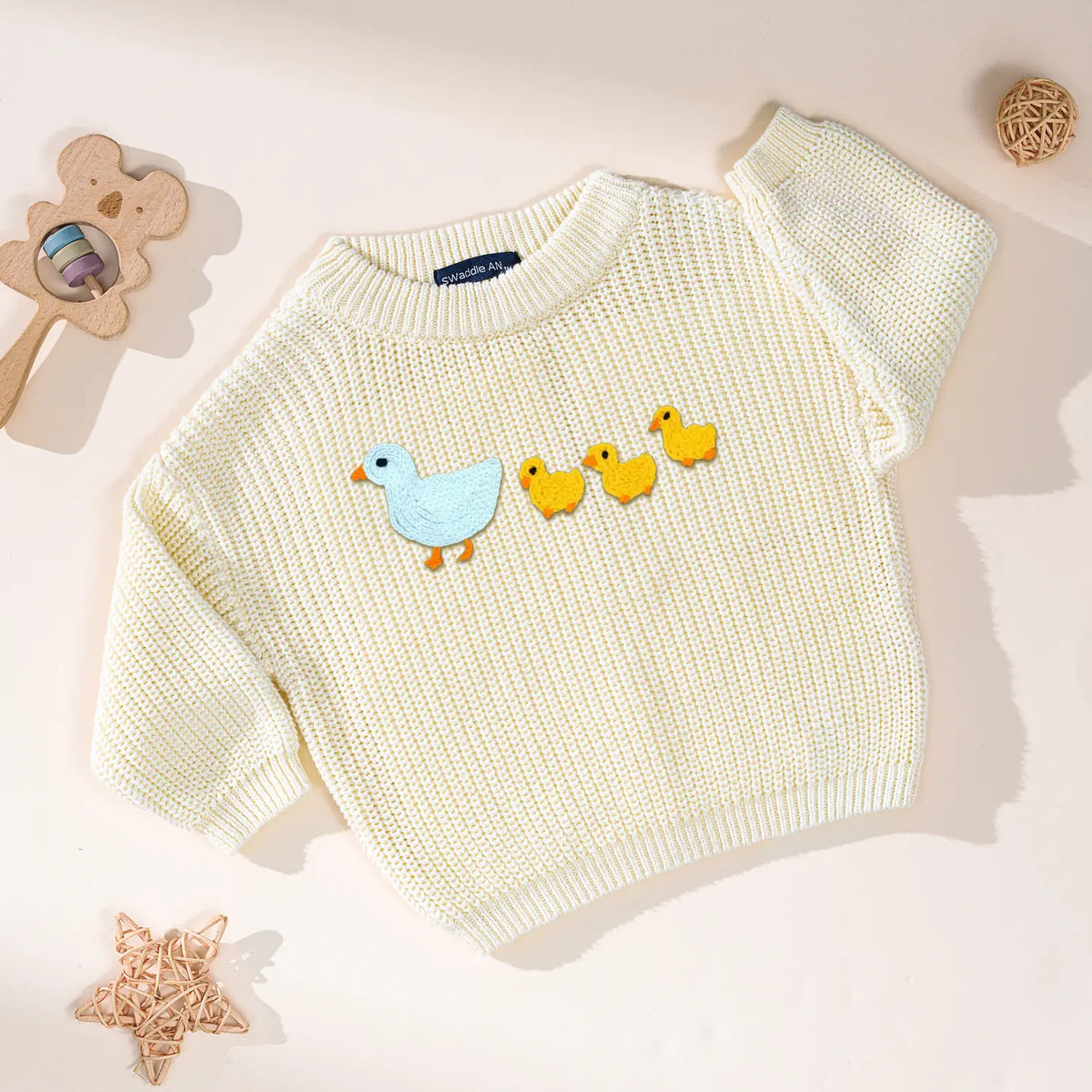Cream colored knit sweater with marching ducks motif beside rattan star prop on neutral backdrop