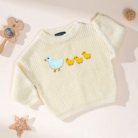 Cream colored knit sweater with marching ducks motif beside rattan star prop on neutral backdrop