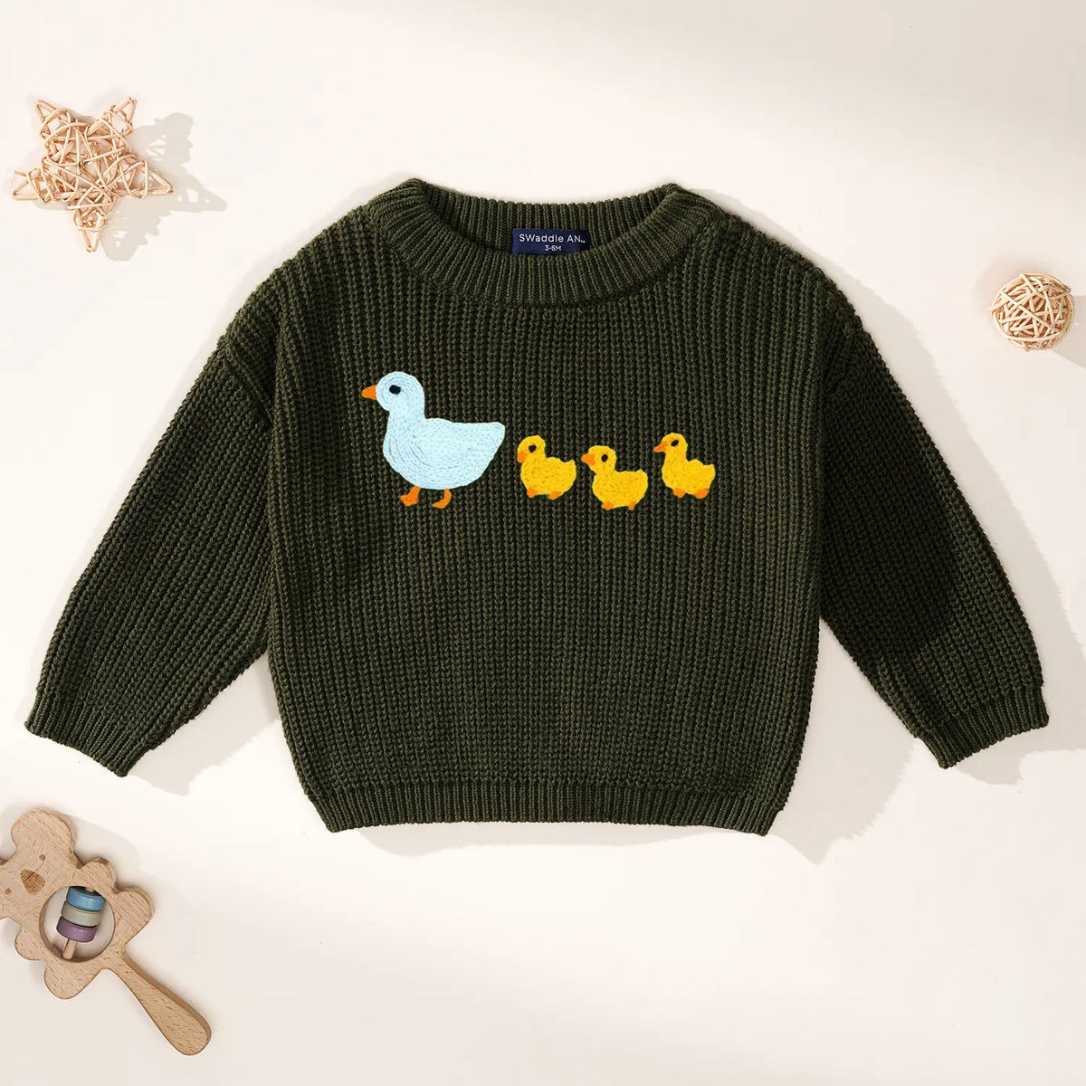 Dark green crewneck sweater with duck embroidery and SWaddle AN tag inside collar with wooden toys