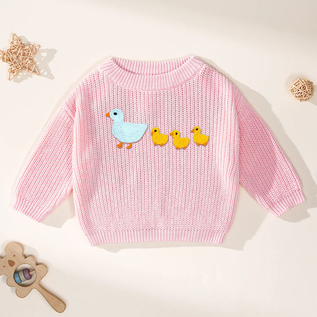 Soft pink long sleeve sweater with blue goose and yellow chicks embroidery next to wooden toys