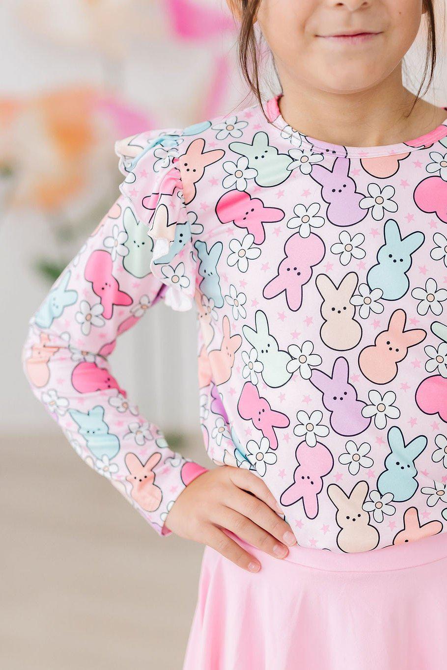 A smiling girl wearing the Hangin with My Peeps L/S Ruffle Tee by Mila & Rose, showcasing a colorful bunny print with flowers, perfect for playful outfits.