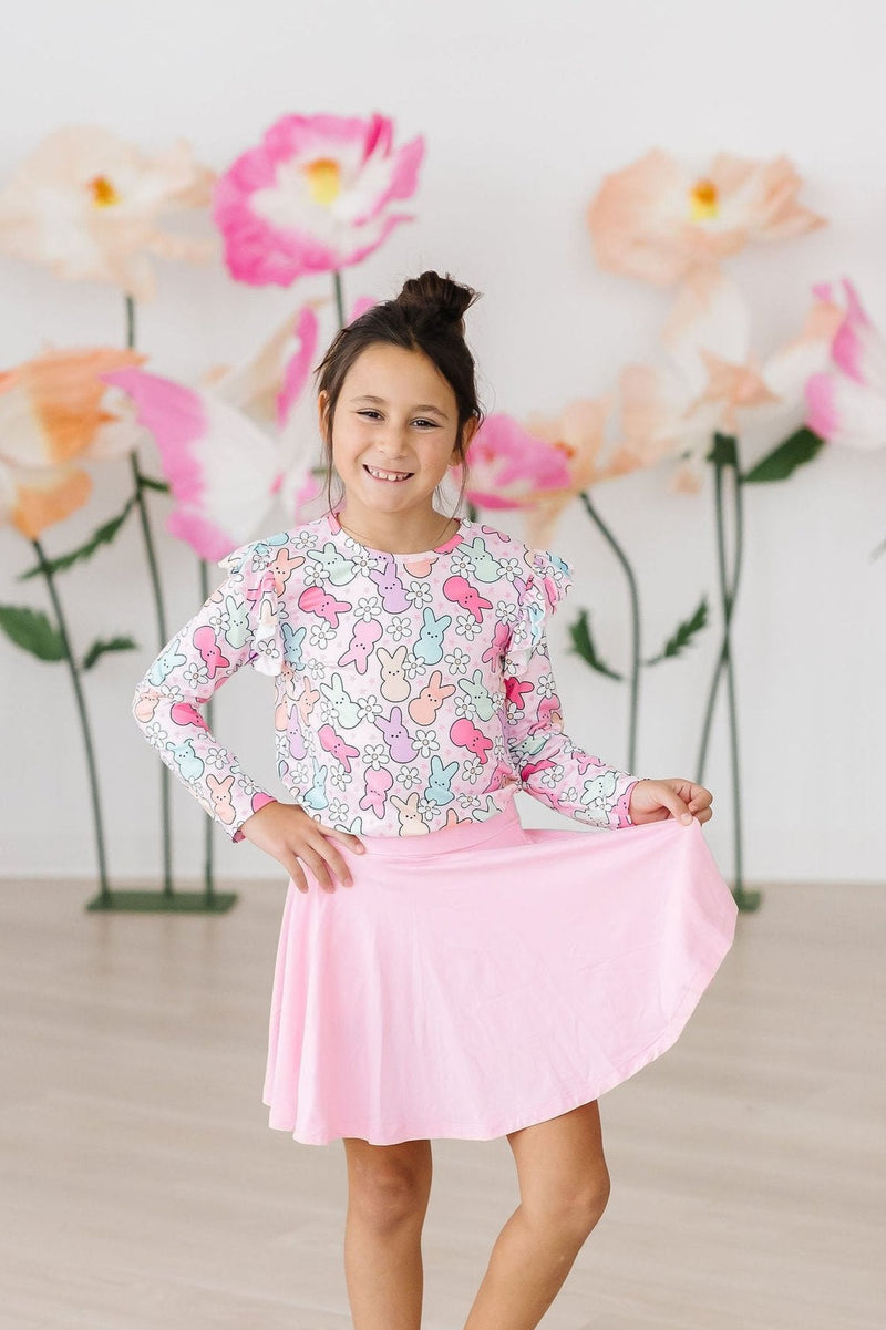 A joyful girl twirling in the Hangin with My Peeps L/S Ruffle Tee by Mila & Rose, featuring a cheerful bunny pattern, paired beautifully with a pink skirt for a cute casual look.