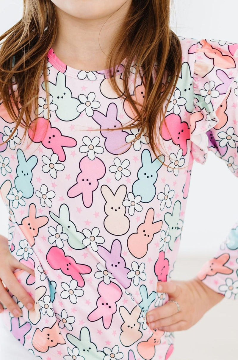 Close-up of a girl's outfit featuring the Hangin with My Peeps L/S Ruffle Tee by Mila & Rose, showcasing cute bunny motifs and floral designs. The image emphasizes the vibrant colors and ruffle details, perfect for children's style.
