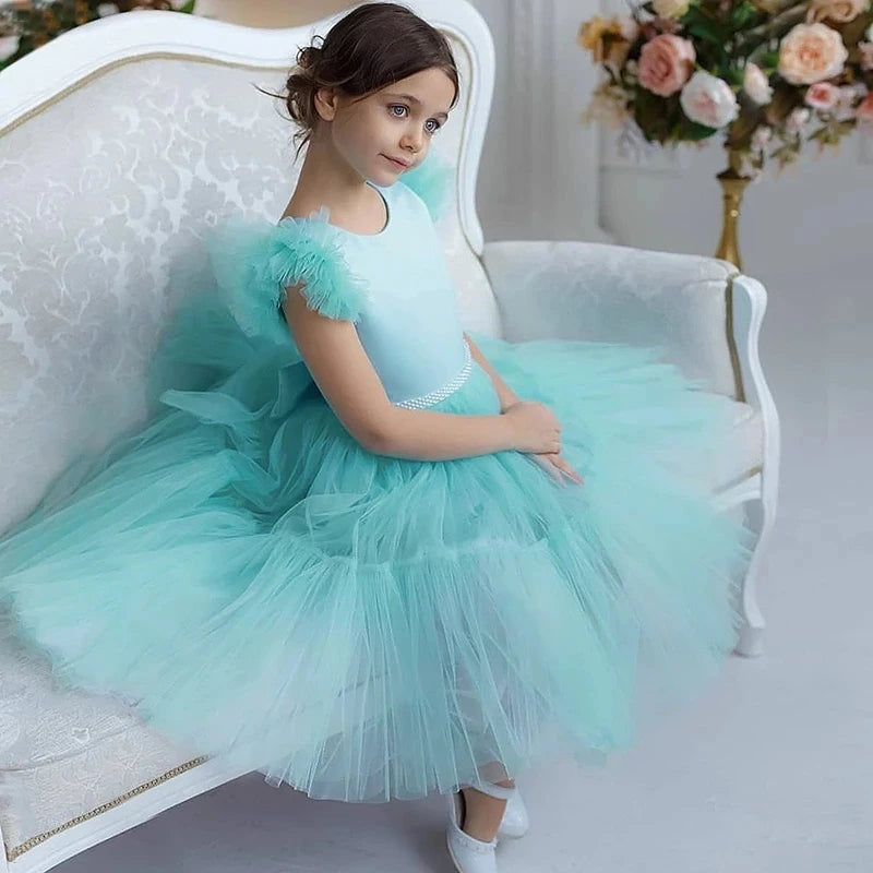 Pretty In Tulle Girls Tulle Party Dress in mint green worn by a young girl, sitting elegantly on a chair, showcasing the oversized bow and twirl-friendly design.