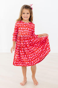 Girl twirling in a red 3/4 sleeve pocket dress with pink hearts. Soft full skirt perfect for play and special occasions.