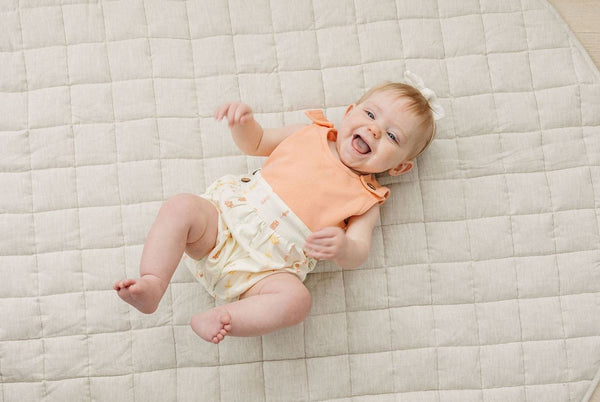 Happy baby lying on a quilt wearing a GOTS certified organic cotton bubble romper with a peach top and boho floral printed bottom.