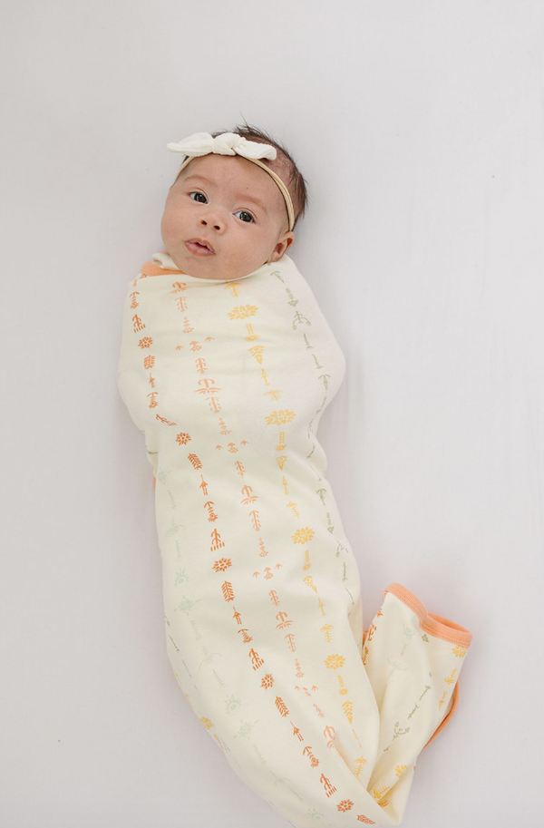 Baby wrapped in GOTS certified organic cotton blanket with boho floral print and peach trim. Chemically safe swaddle for infants.