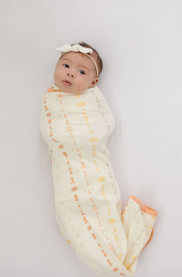 Baby wrapped in GOTS certified organic cotton blanket with boho floral print and peach trim. Chemically safe swaddle for infants.