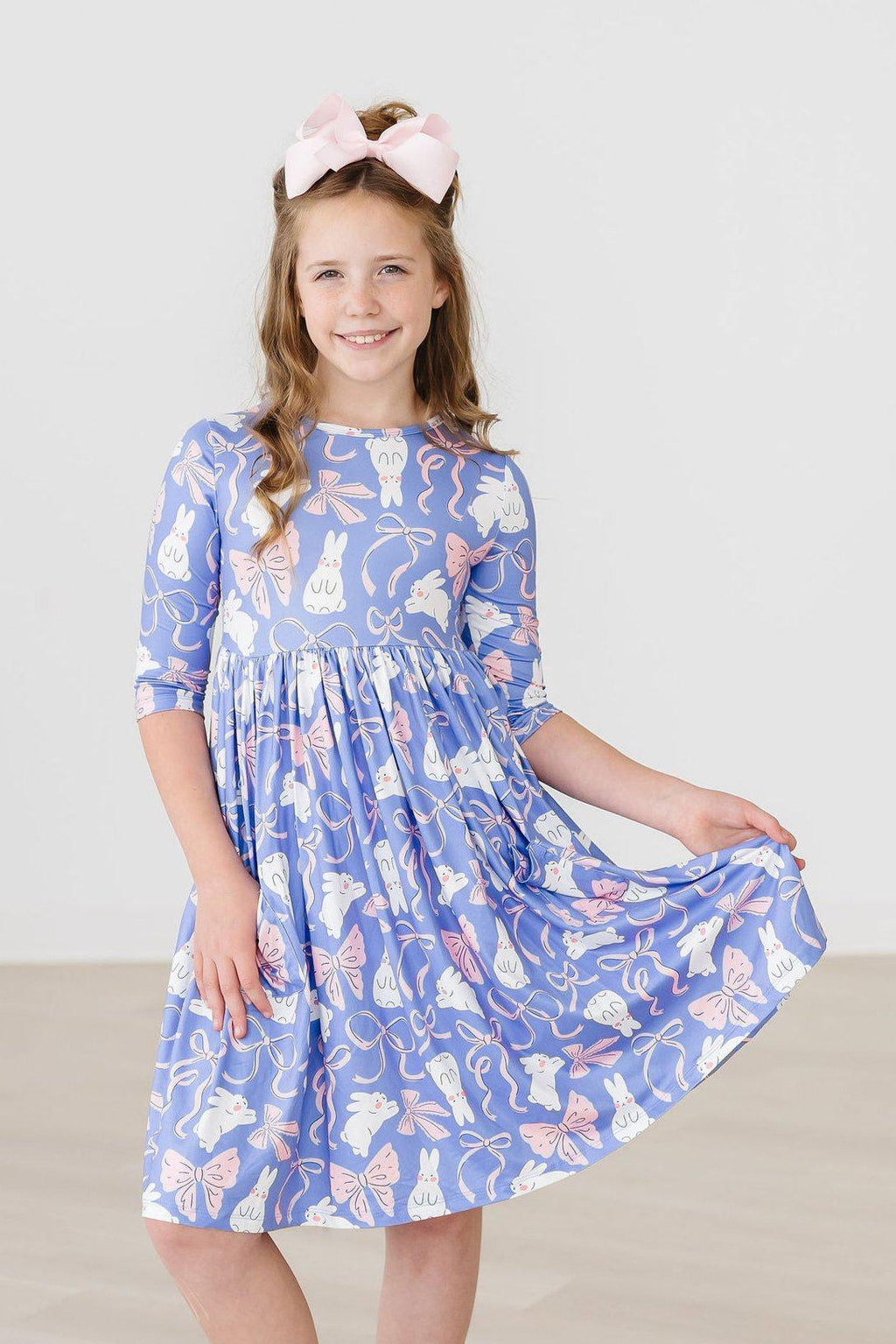 Hop, Skip & Twirl 3/4 Sleeve Pocket Twirl Dress worn by a girl smiling, showcasing a playful bunny and bow pattern, perfect for fun adventures.