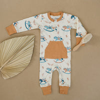 GOTS certified organic cotton baby playsuit with rocking horse print and front pocket, laid flat with dried leaf and brush.