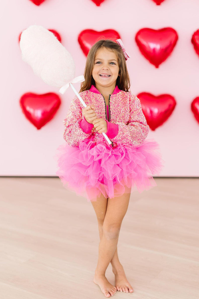 Playful child in a Hot Pink Sequin Jacket from Mila & Rose, twirling with joy while holding cotton candy in a tutu, surrounded by heart balloons for a whimsical touch.