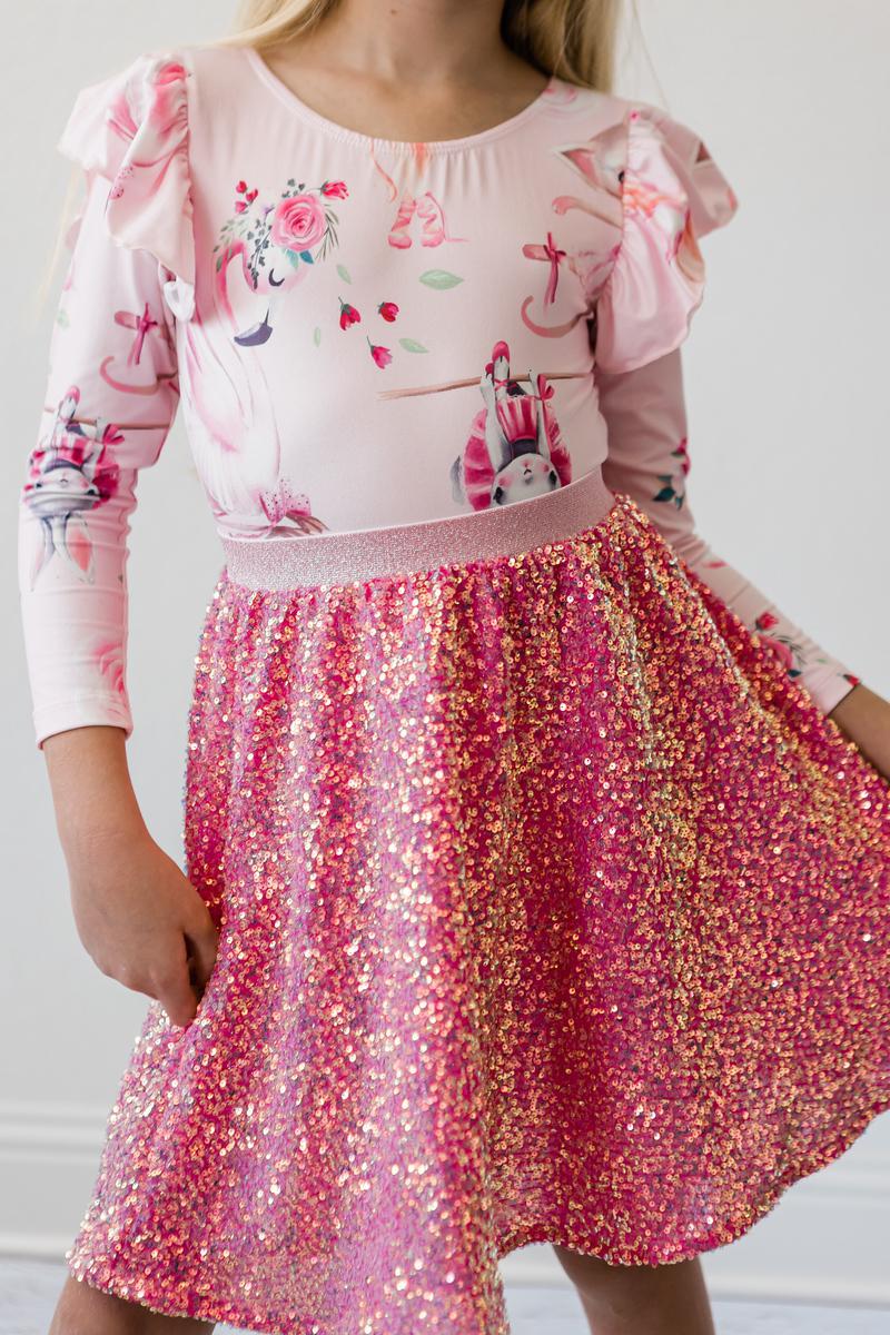 A stylish young girl wearing the Hot Pink Sequin Twirl Skort from Mila & Rose, showing off the vibrant, sparkly fabric as she poses with a playful flair. Perfect for twirling and dancing at special occasions!