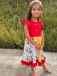 Girl in red top and pencil patchwork twirl dress with ruffles, school-print skirt outdoors.
