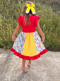 Back view of a girl in a red top wearing a patchwork pencil twirl dress with ruffles and a yellow bow.
