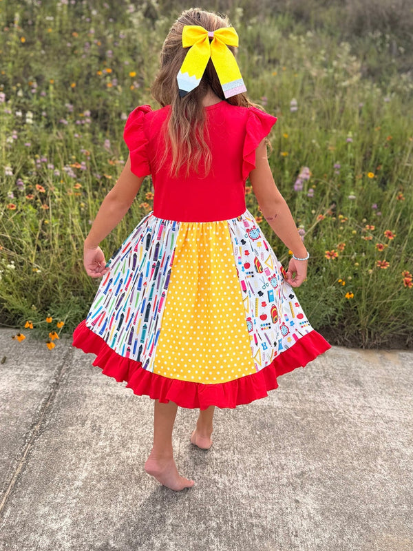 Back view of a girl in a red top wearing a patchwork pencil twirl dress with ruffles and a yellow bow.