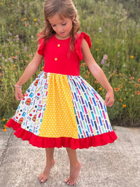 Girl wearing a bright back-to-school pencil patchwork twirl dress with red ruffle sleeves.