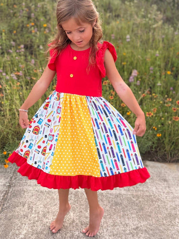 Girl wearing a bright back-to-school pencil patchwork twirl dress with red ruffle sleeves.