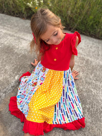 Girl wearing a back-to-school pencil patchwork twirl dress with red bodice and ruffled hem.