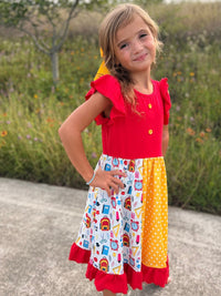 Girl wearing a bright patchwork twirl dress with red top, ruffled sleeves, and school-themed prints