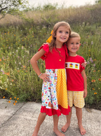 Two kids outdoors in red tops; boy in yellow plaid shorts from Back to School Crayon Smocked Boys Plaid Shorts Set.