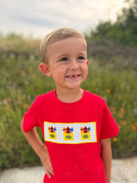 Young boy in a red shirt with a crayon-smocked patch outdoors, school-themed outfit.