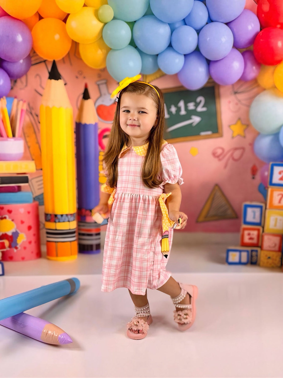 Girls Back To School Pencil Twirl Dress with bow appliques, worn by a smiling girl in front of colorful balloons and school supplies.