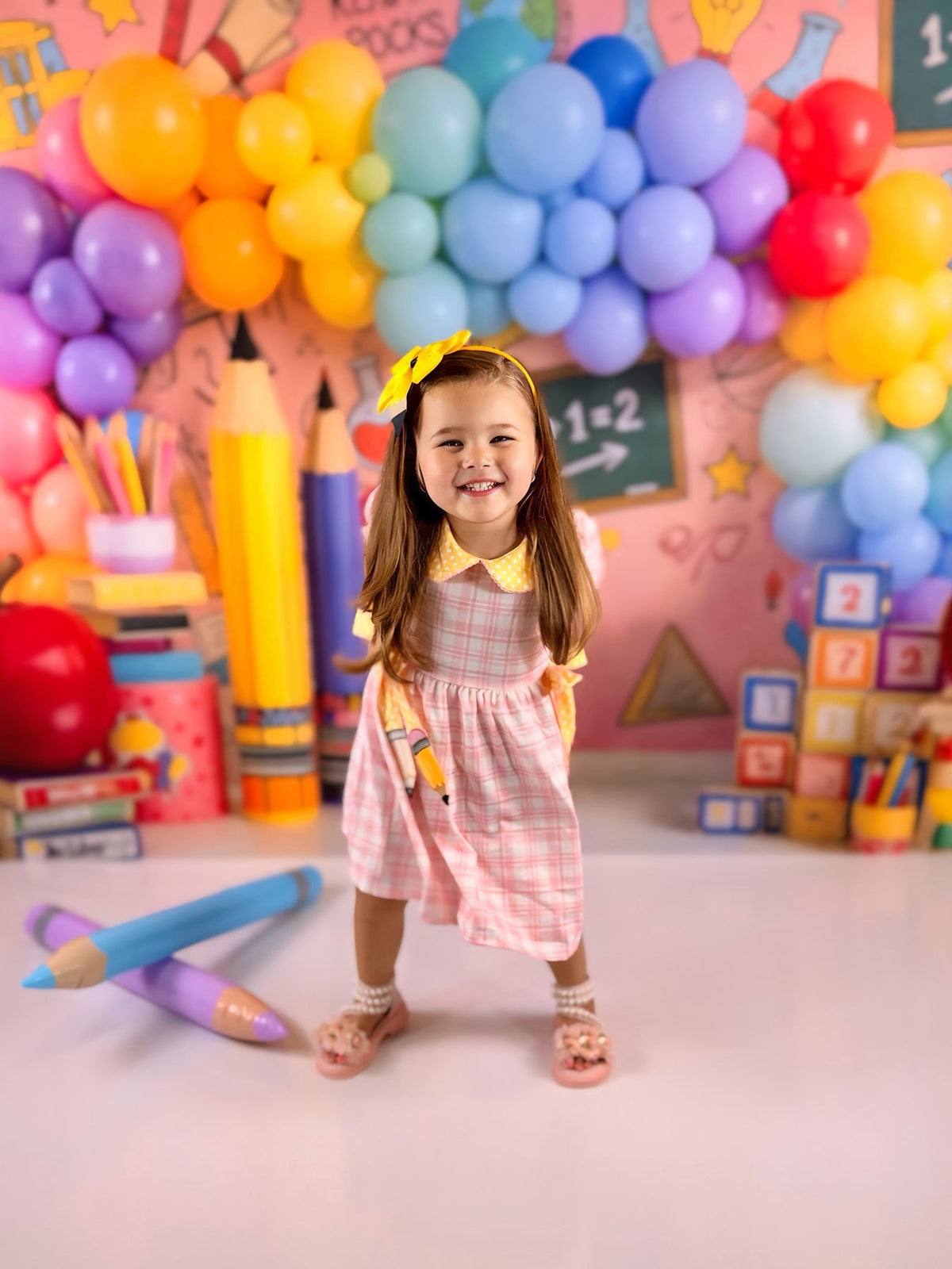 Happy girl in a Girls Back To School Pencil Twirl Dress, twirling with joy in a vibrant school-themed setting with balloons.