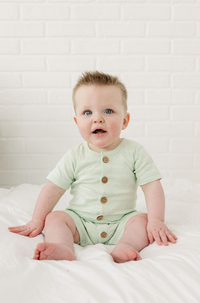 Baby wearing GOTS certified organic cotton short sleeve romper in Desert Green with "I Love You" print and wooden buttons.