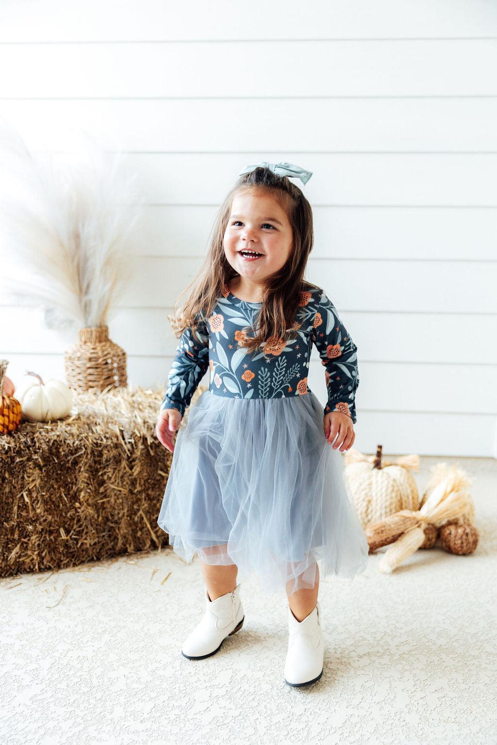 Smiling girl in floral long sleeve tutu dress and white boots near hay bales and pumpkins. Perfect dress for play or special occasions.