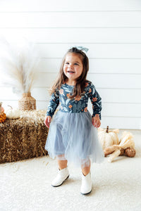 Smiling girl in floral long sleeve tutu dress and white boots near hay bales and pumpkins. Perfect dress for play or special occasions.