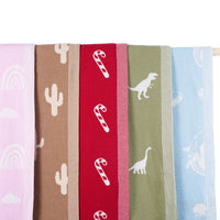 Five hanging baby blankets displaying lilac rainbows, brown cacti, red candy canes, olive dinosaurs, and blue marine life